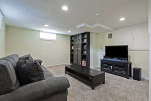 Living area with a textured ceiling, baseboards, carpet floors, and recessed lighting