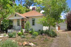 View of front of house with a chimney, a detached garage, an outbuilding, driveway, and a shingled roof
