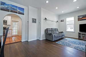 Living area with dark wood-style floors, crown molding, recessed lighting, arched walkways, and baseboards