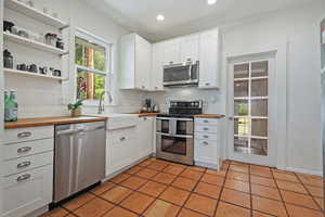 Kitchen with appliances with stainless steel finishes, butcher block countertops, a sink, backsplash, and white cabinets
