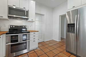 Kitchen featuring appliances with stainless steel finishes, butcher block counters, backsplash, white cabinetry, and light tile patterned flooring
