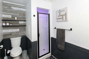 Full bathroom featuring crown molding, a shower stall, toilet, wooden walls, and wainscoting