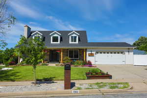 Cape cod house with a garage, a front yard, concrete driveway, a chimney, and stone siding