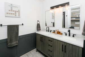 Bathroom with double vanity, crown molding, wood finished floors, and a wainscoted wall