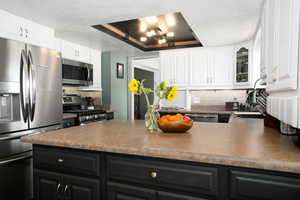 Kitchen with appliances with stainless steel finishes, dark cabinetry, a textured ceiling, dark countertops, and white cabinetry