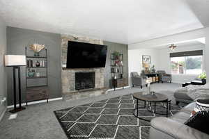 Carpeted living area with baseboards, a stone fireplace, and a textured ceiling