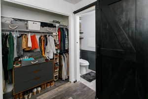 Bathroom with wood finished floors, toilet, a walk in closet, and a wainscoted wall