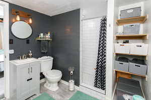 Full bathroom featuring tiled shower, vanity, toilet, a textured ceiling, and baseboards