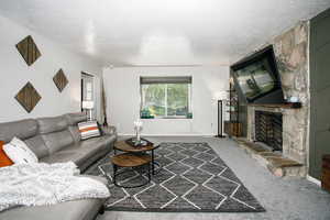 Living room featuring a textured ceiling, a fireplace, carpet floors, and baseboards