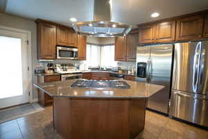 Kitchen with stainless steel appliances, island exhaust hood, a sink, recessed lighting, and dark stone counters