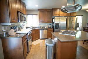 Kitchen featuring stainless steel appliances, island range hood, a sink, light tile patterned floors, and a center island