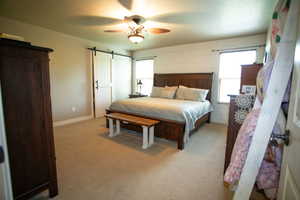 Bedroom with a barn door, carpet, baseboards, and ceiling fan