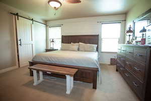 Bedroom with a barn door, light carpet, and baseboards