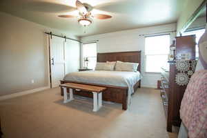 Bedroom with a barn door, light carpet, ceiling fan, and baseboards