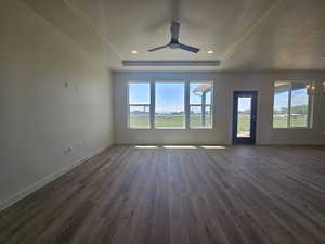 Unfurnished living room with dark wood-style flooring, healthy amount of natural light, baseboards, a textured ceiling, and a tray ceiling