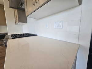 Kitchen view of light stone countertops, stainless steel microwave, stovetop, exhaust hood, and tasteful backsplash
