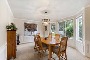 Dining area featuring light carpet, healthy amount of natural light, a decorative wall, ornamental molding, and a chandelier