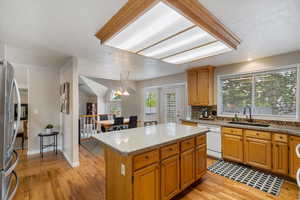 Kitchen with white dishwasher, a sink, light wood-style floors, and a kitchen island