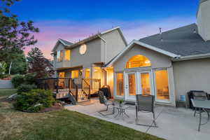 Back of house at dusk featuring stucco siding, a patio, a deck, and a shingled roof