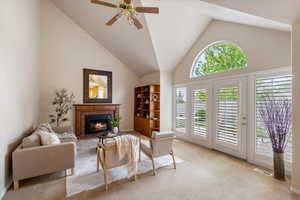 Carpeted living room featuring healthy amount of natural light, a brick fireplace, ceiling fan, high vaulted ceiling, and baseboards