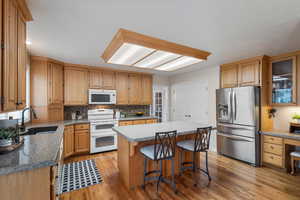 Kitchen featuring white appliances, a sink, light wood-style floors, backsplash, and a breakfast bar