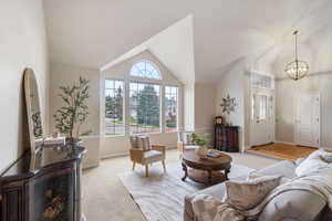 Living area featuring a chandelier, baseboards, high vaulted ceiling, and light carpet