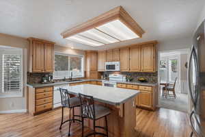 Kitchen with white appliances, a sink, light wood-style flooring, a kitchen island, and decorative backsplash