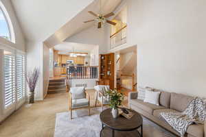 Living area with high vaulted ceiling, stairway, light carpet, baseboards, and a chandelier
