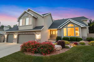 Traditional-style home with stucco siding, stone siding, a garage, driveway, and roof with shingles