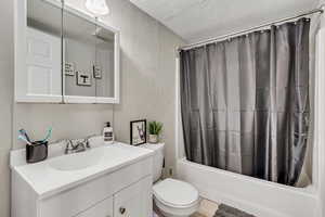 Full bath with a textured wall, vanity, shower / tub combo with curtain, toilet, and a textured ceiling