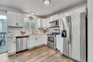 An open concept kitchen with appliances with stainless steel finishes, a sink, white cabinets, and contemporary laminate flooring