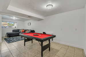 Recreation room featuring baseboards, billiards, light tile patterned flooring, and a textured ceiling