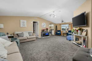 Living room featuring carpet, a ceiling fan, vaulted ceiling, and a chandelier