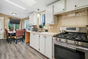 Kitchen featuring stainless steel gas range, a sink, a skylight, vaulted ceiling, and light wood-type flooring