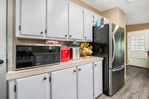 Kitchen with freestanding refrigerator, light wood-style flooring, light countertops, and white cabinetry