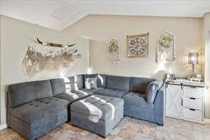 Living area with vaulted ceiling, light stone finish floors, and attic access
