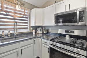 Kitchen featuring stainless steel appliances, a sink, white cabinets, lofted ceiling, and dark stone countertops