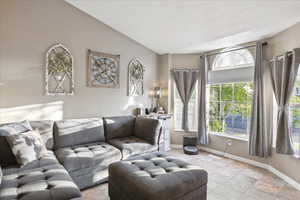 Living area featuring baseboards, light tile patterned floors, and lofted ceiling