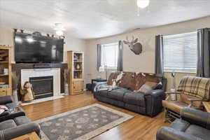 Living area featuring a ceiling fan, a textured ceiling, wood finished floors, and a fireplace