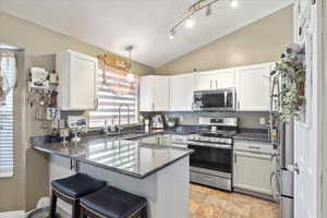 Kitchen featuring stainless steel appliances, a sink, a peninsula, lofted ceiling, and white cabinets