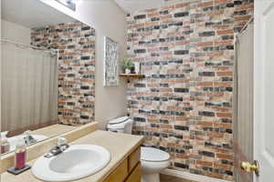 Bathroom featuring vanity, toilet, brick wall, and curtained shower