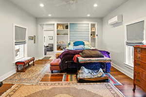 Bedroom with recessed lighting, wood finished floors, a wall unit AC, baseboards, and multiple windows