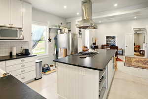 Kitchen featuring stainless steel appliances, dark countertops, island range hood, a center island, and tasteful backsplash