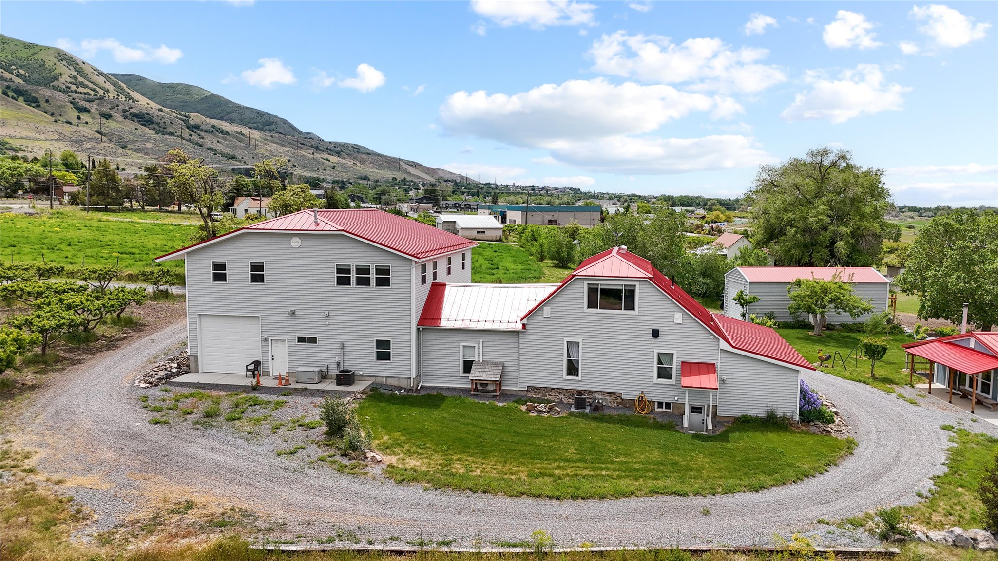 Back of property with dirt driveway, a mountain view, metal roof, a lawn, and a garage