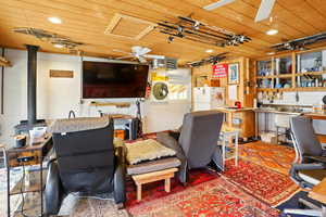 Office area with ceiling fan, a wood stove, wooden ceiling, and concrete block wall