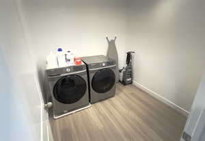Washroom with washing machine and clothes dryer, wood finished floors, and baseboards