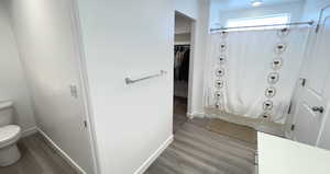 Full bathroom with toilet, wood finished floors, baseboards, and a shower with curtain