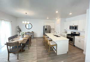 Kitchen featuring stainless steel appliances, a sink, a chandelier, a breakfast bar area, and a kitchen island with sink