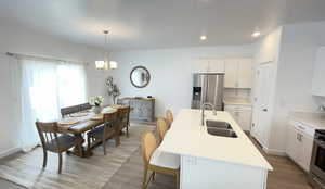 Kitchen with stainless steel fridge, a sink, a chandelier, white cabinetry, and light wood-style floors