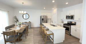 Kitchen with appliances with stainless steel finishes, a sink, wood finished floors, a chandelier, and a breakfast bar